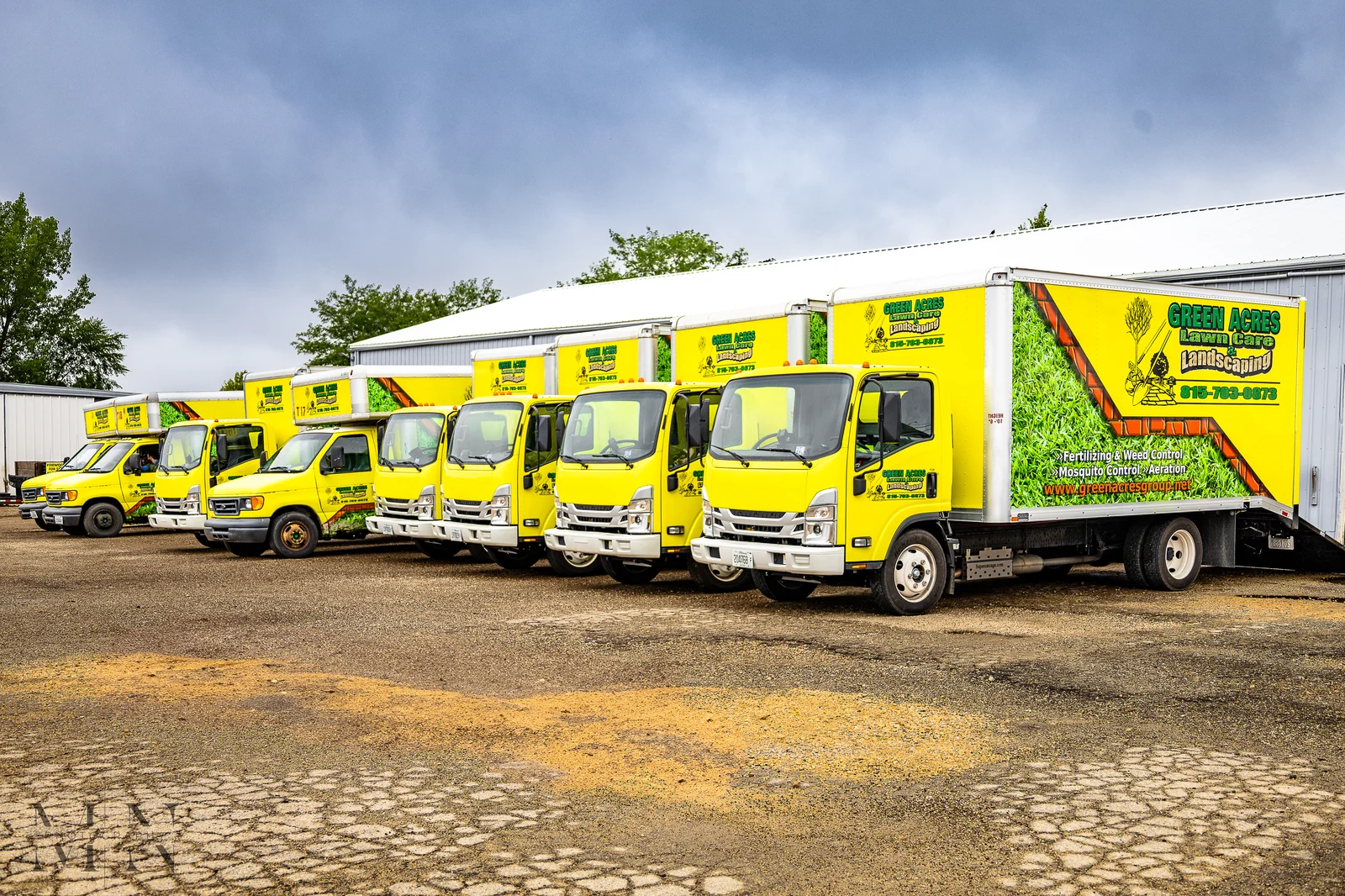 Green Acres Landscaping fleet of yellow branded box trucks and vans lined up at company facility