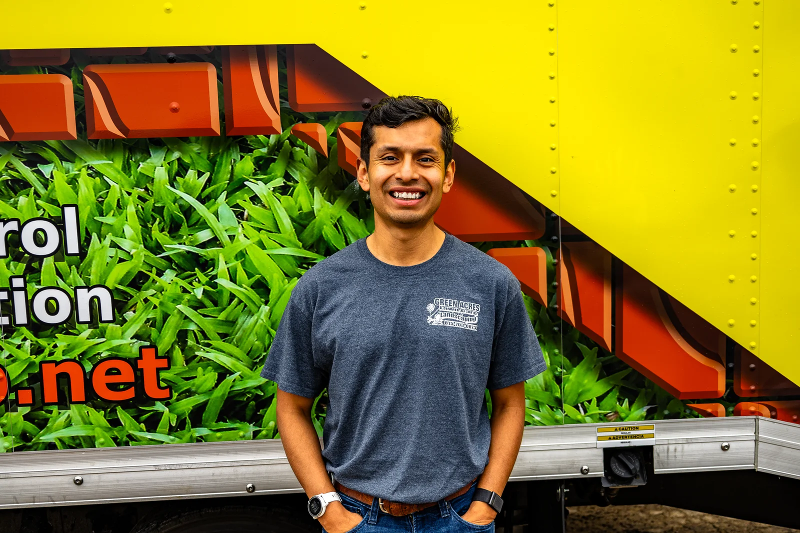 Green Acres landscaping team member standing in front of company branded trailer with lawn graphics