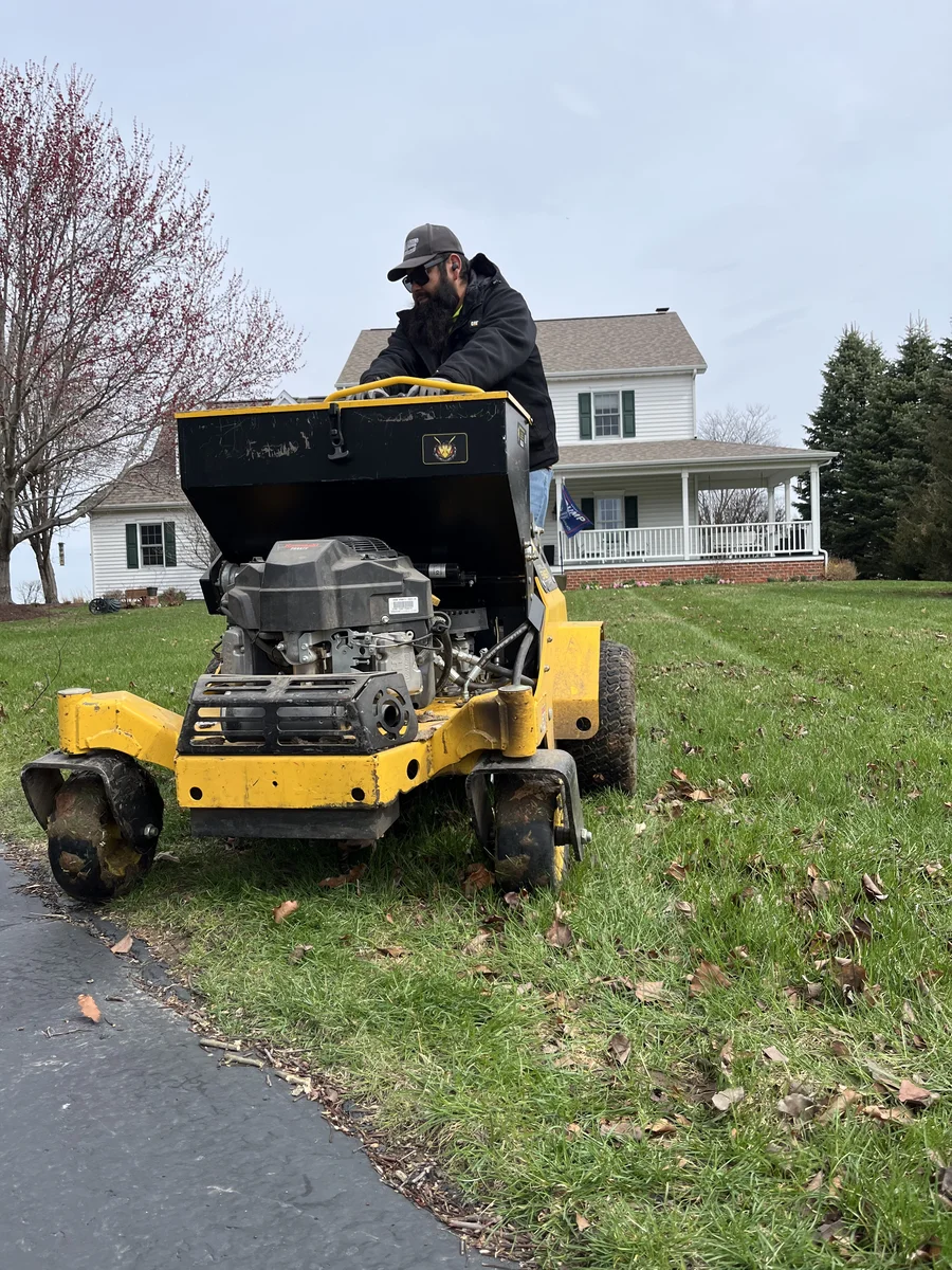 Green Acres crew member performing overseeding service on residential lawn with yellow stand-on seeder