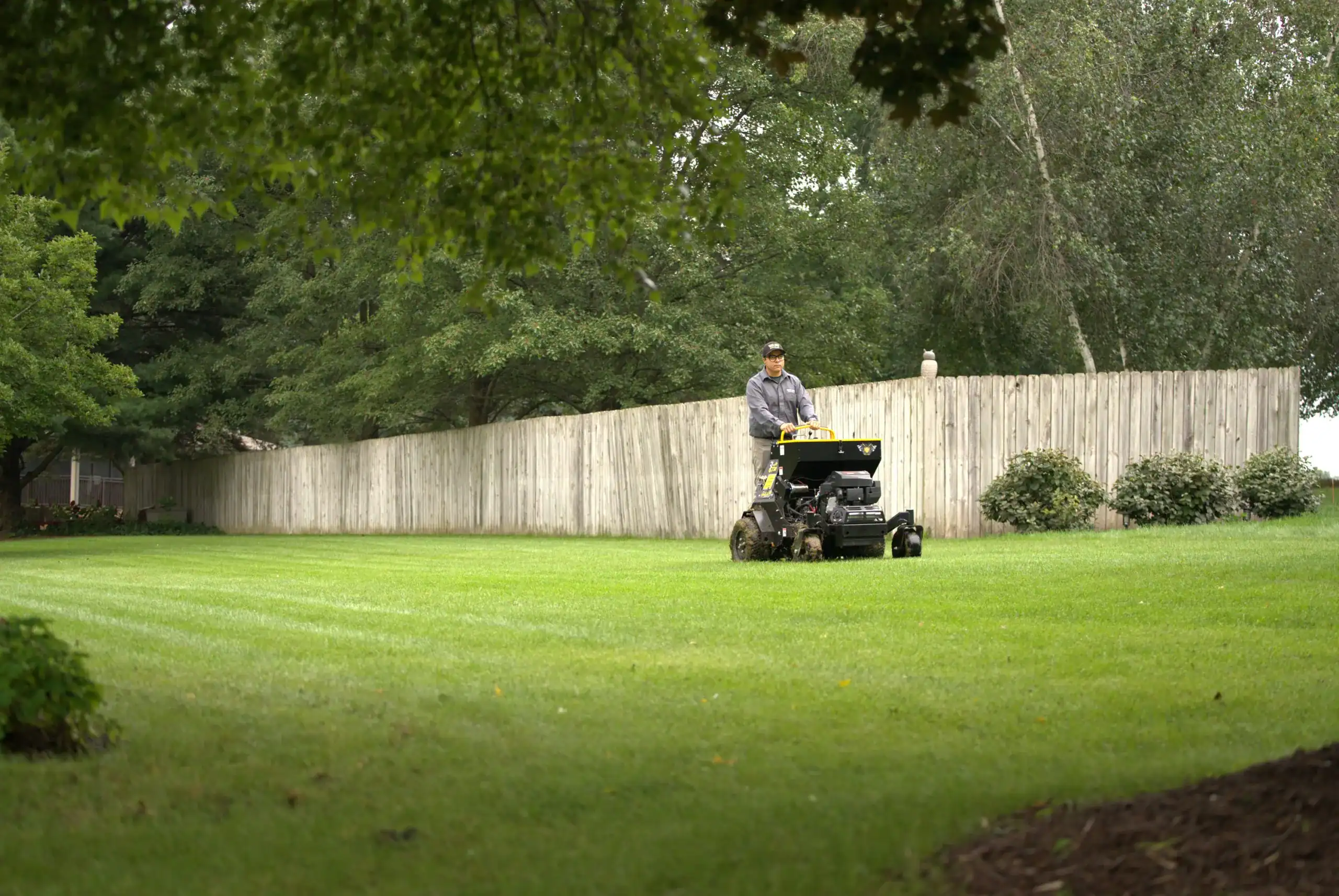 Green Acres crew member performing lawn care fertilization service with stand-on spreader on residential property