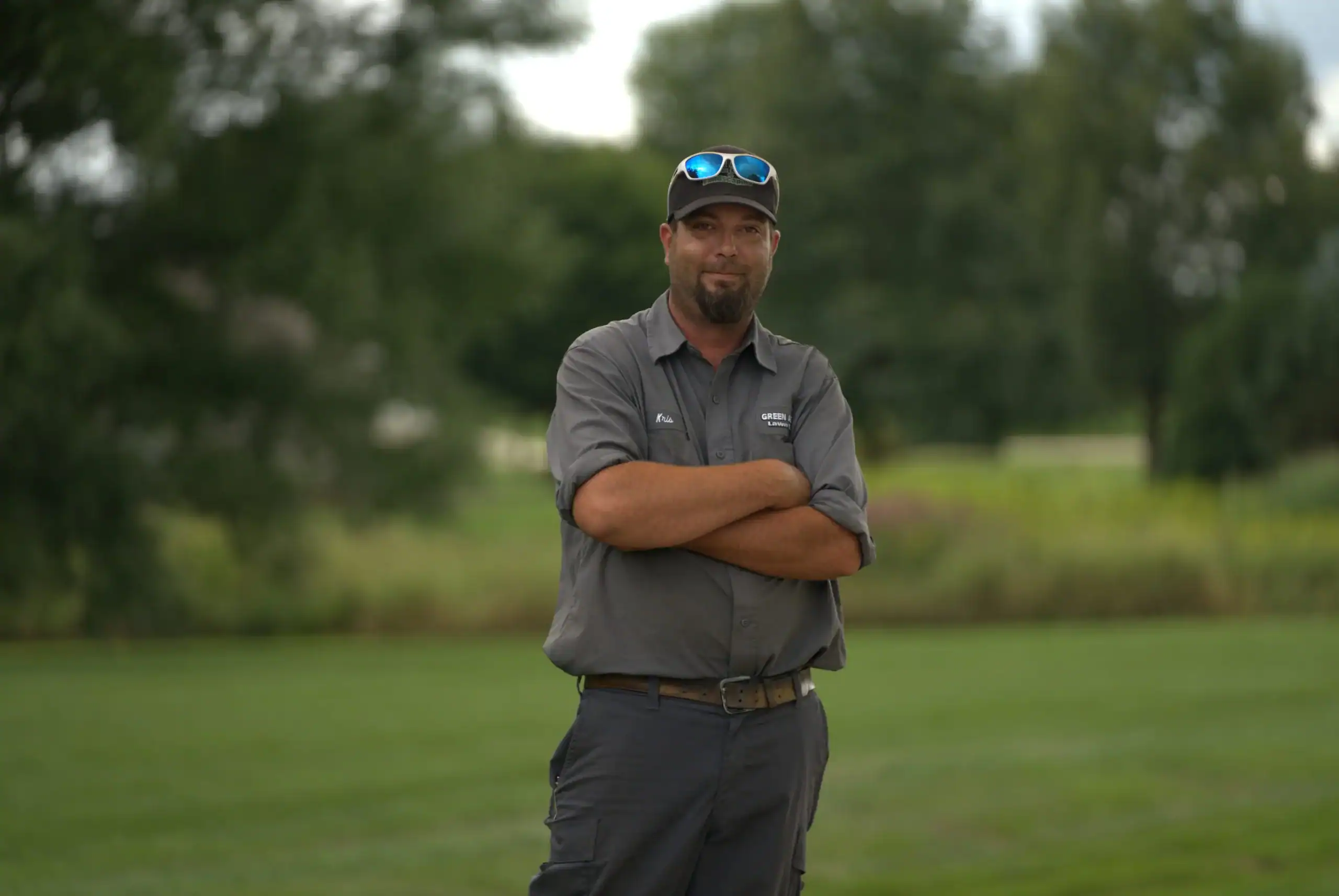 Green Acres landscaping crew member standing confidently on well-maintained lawn