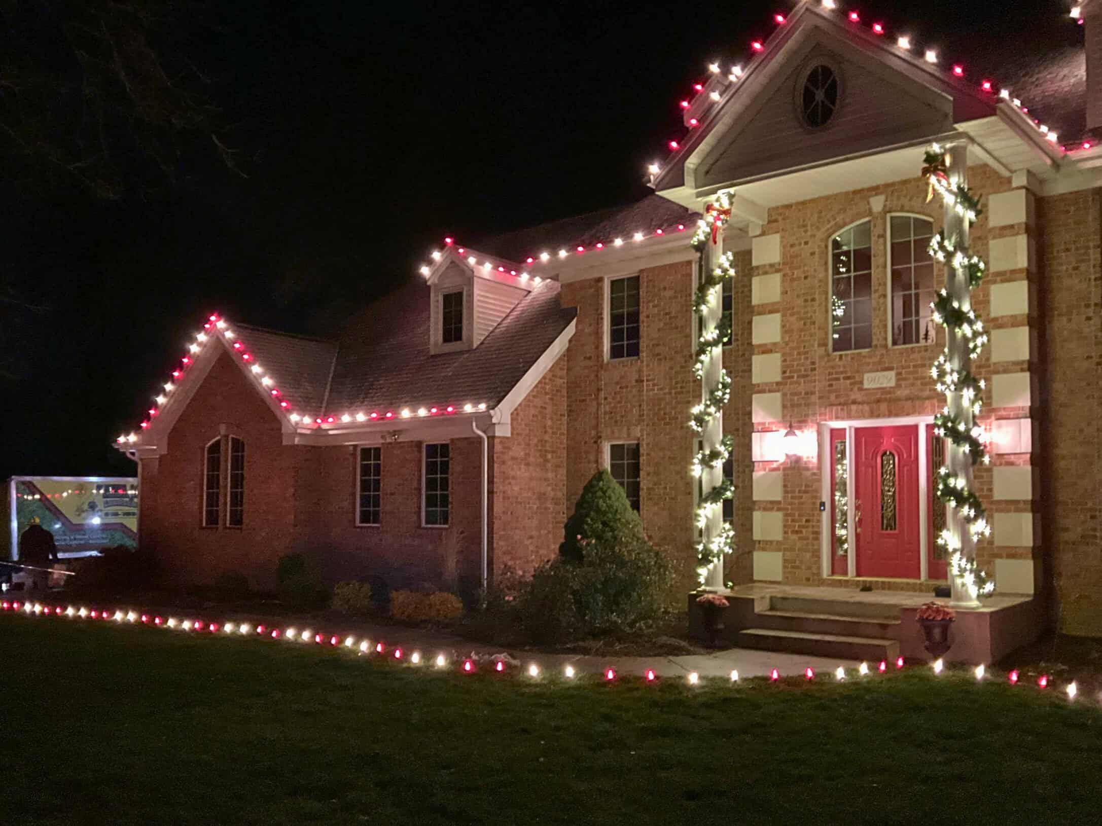 Green Acres holiday lighting installation on residential brick home with red and white lights